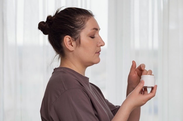 Brunette woman puts moisturizing cream on face at home