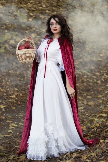 Brunette woman in red cloak in the woods, woman in magical forest with smoke, vertical photo