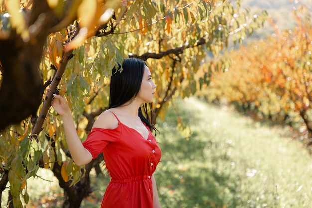 Brunette woman in red dress posing against trees.