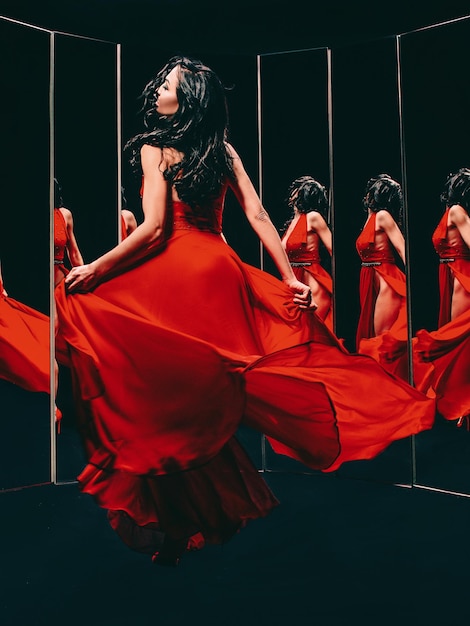 brunette woman in red shoes and dress turning around and dancing near the mirror