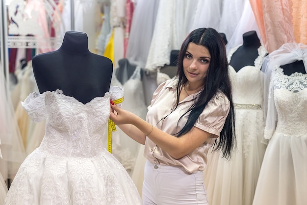 Brunette woman seller measuring details of wedding dress