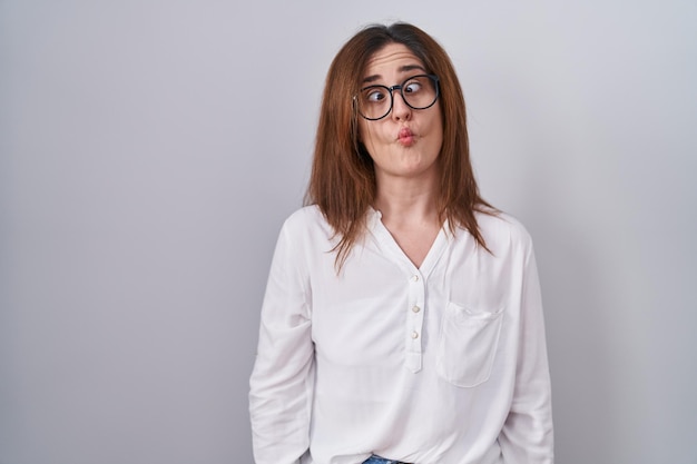 Brunette woman standing over white isolated background making fish face with lips crazy and comical gesture funny expression