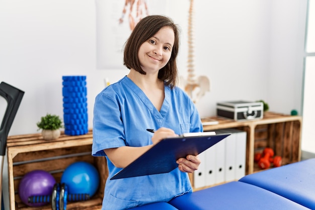 Brunette woman with down syndrome working holding clipboard at physiotherapy clinic