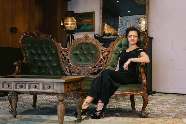 Brunette woman with hairstyle in black clothes sits on a sofa