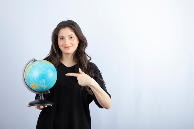 Brunette woman with long hair holding world globe and posing . 