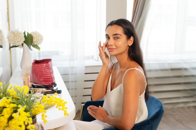 Brunette woman with long straight dark hair and clean skin doing make up routine