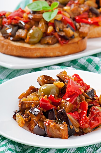 Bruschetta caponata with raisins and pine nuts decorated with a leaf of basil