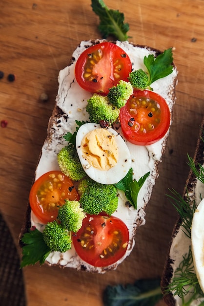 Bruschetta on dark bread curd cheese halves of cherry tomatoes pieces of broccoli parsley and spices