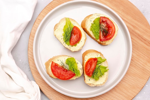 Bruschetta sandwich bread toast with soft white cheese ricottafresh tomatoesbasil greenery on a wooden cutting boardTasty healthy vegetarian foodItalian cuisine appetizer top view flat lay