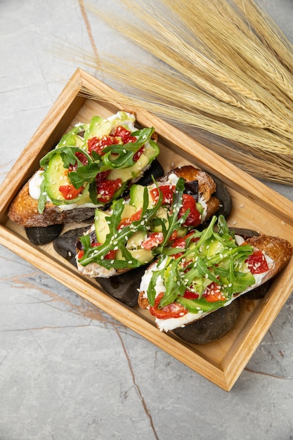 Bruschetta with avocado feta arugula peppers and tomatoes on a gray table