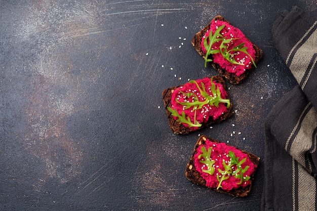 Bruschetta with beetroot hummus, arugula and sesame seeds on dark concrete surface