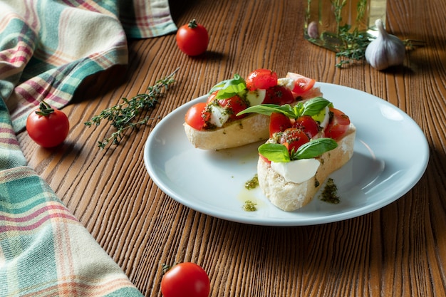 Bruschetta with cherry tomatoes, basil, pesto sauce and mozzarella on a white plate on a wooden background. I