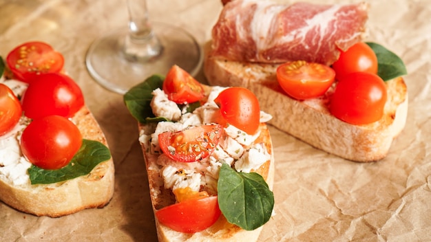 Bruschetta with cherry tomatoes. Wine glass, Italian appetizer. Craft paper background. Set of three bruschettes. Picnic concept