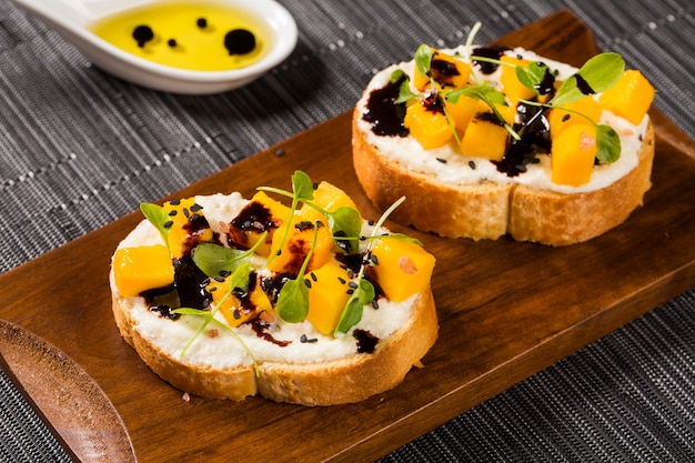 Bruschetta with chopped mango, cress, basil and goat cheese on fresh baguette on the table