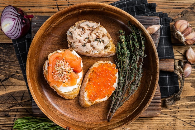 Bruschetta with Hot Smoked salmon, red caviar and herbs. Wooden background. Top view.