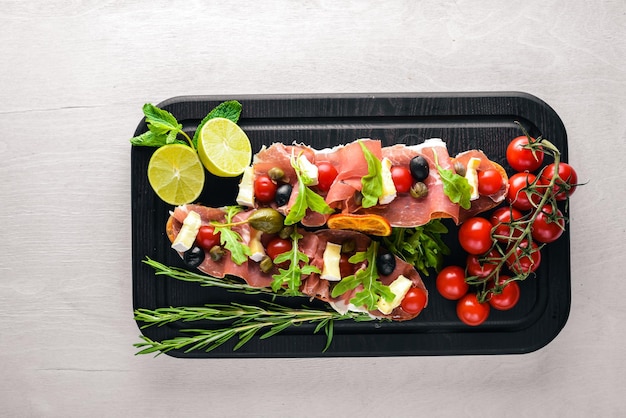 Bruschetta with meat, olives, herbs and parmesan cheese on bread. Cold snacks. Italian cuisine. On Wooden background.