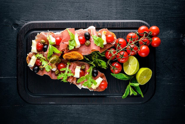 Bruschetta with meat olives herbs and parmesan cheese on bread Cold snacks Italian cuisine On Wooden background