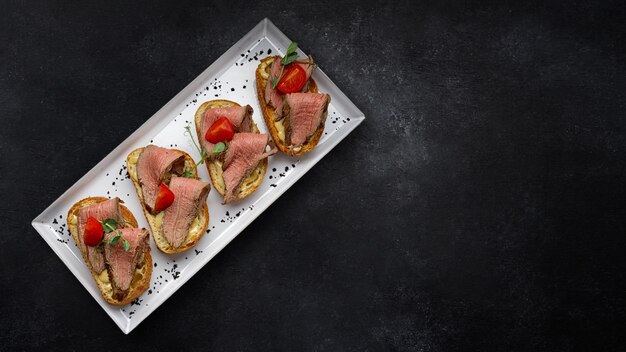 Bruschetta with meat sauce and tomatoes on a dark background