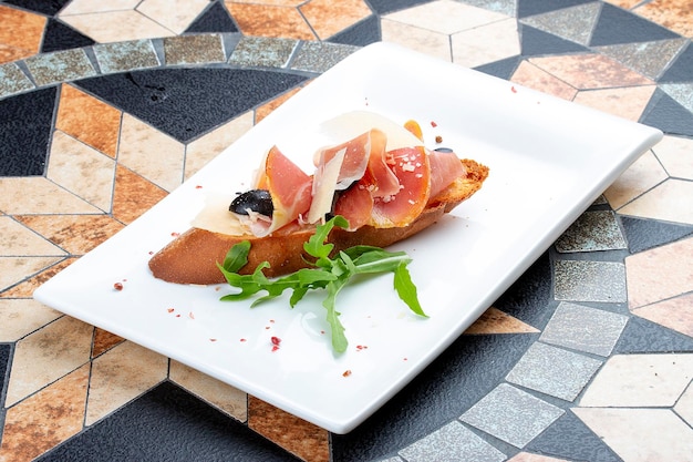 Bruschetta with prosciutto and arugula on a white plate