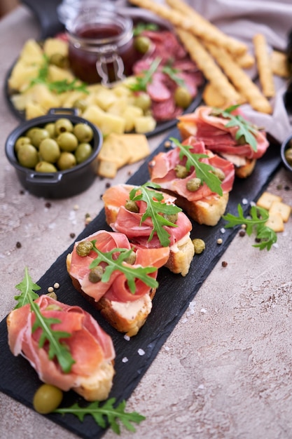 Bruschetta with prosciutto ham and capers with traditional antipasto meat plate on background