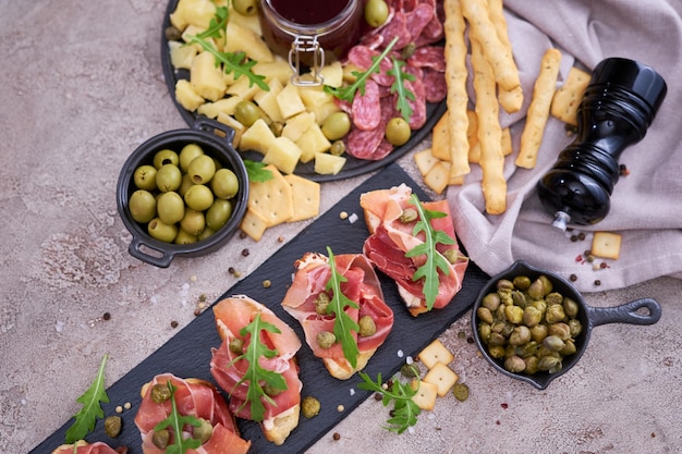 Bruschetta with prosciutto ham and capers with traditional antipasto meat plate on background