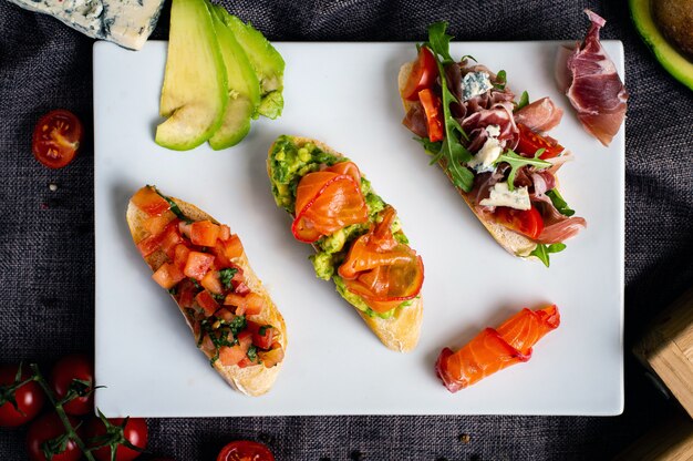 Bruschetta with salmon, veal, tomatoes, avocado. Assorted sandwiches. The laid out ingredients on the side. Top view.