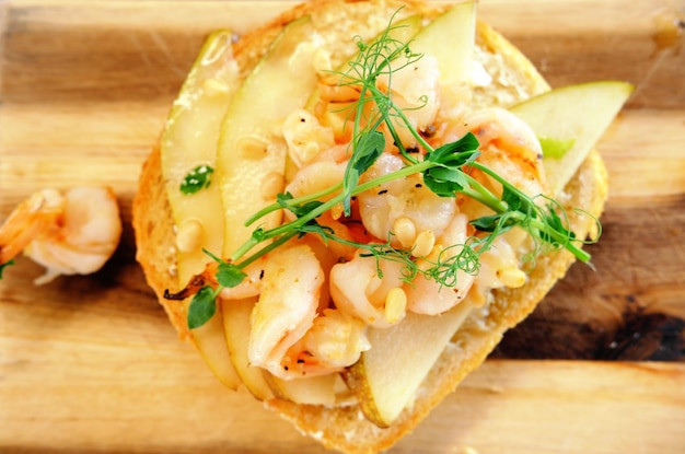 Bruschetta with shrimp pear and pine nuts on a wooden board Horizontal photo