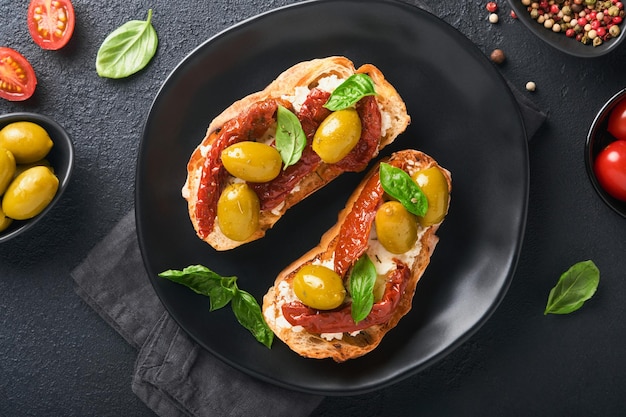 Bruschetta with sun dried tomatoes Toast or sandwich with ricotta sun dried tomatoes and Provence herbs with basil servered on black plate on black background table Top view banner menu recipe