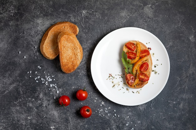 Bruschetta with tomatoes on a white plate against dark background, top view