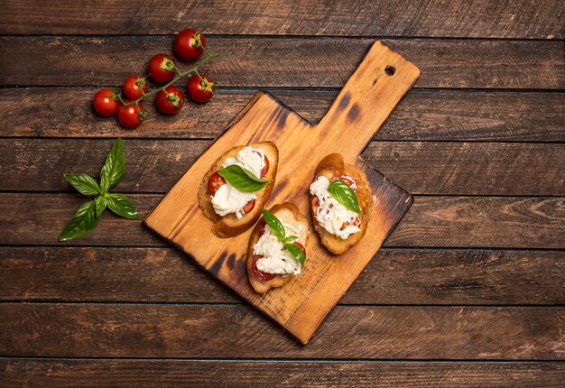 Bruschettas with stracciatella cheese cherry tomatoes and basil on wooden cutting board