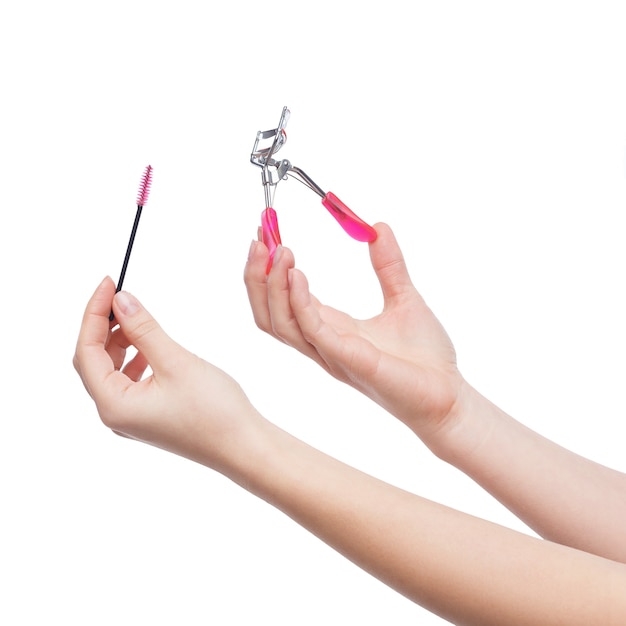 Brush and eyelash curlers in female hands isolated on white background