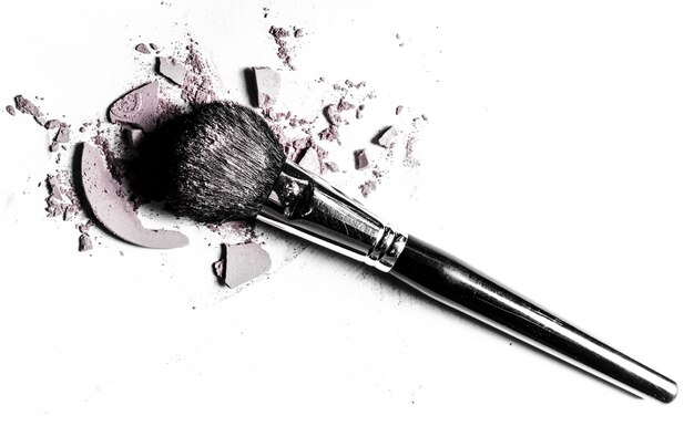 Brush with crushed eyeshadow and powder closeup isolated on white background