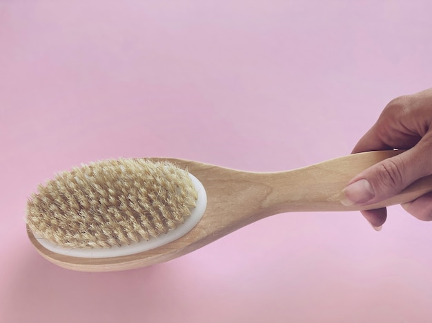 Photo brush with a handle for dry anti-cellulite massage or brushing in the hand of a girl in soft pink colors.  beauty concept.