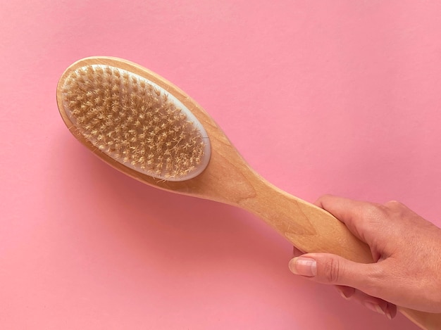 Brush with a handle for dry anti-cellulite massage or brushing in the hand of a girl in soft pink colors.  Beauty concept.