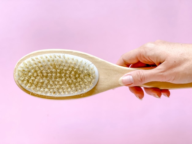 Photo brush with a handle for dry anti-cellulite massage or brushing in the hand of a girl in soft pink colors.  beauty concept.