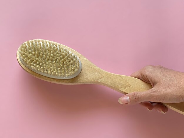 Brush with a handle for dry anti-cellulite massage or brushing in the hand of a girl in soft pink colors.  Beauty concept.