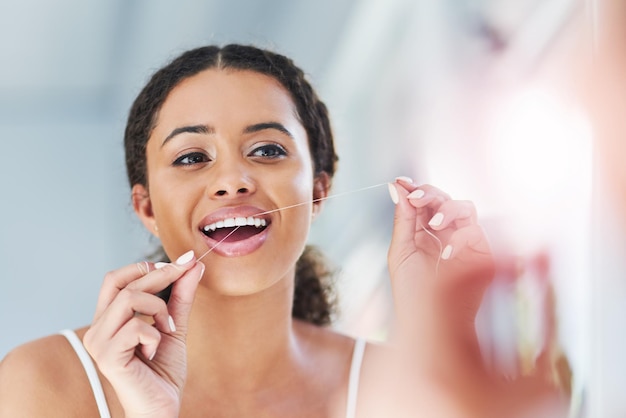 Brushing alone simply wont do it Cropped shot of an attractive young woman flossing her teeth in the bathroom at home