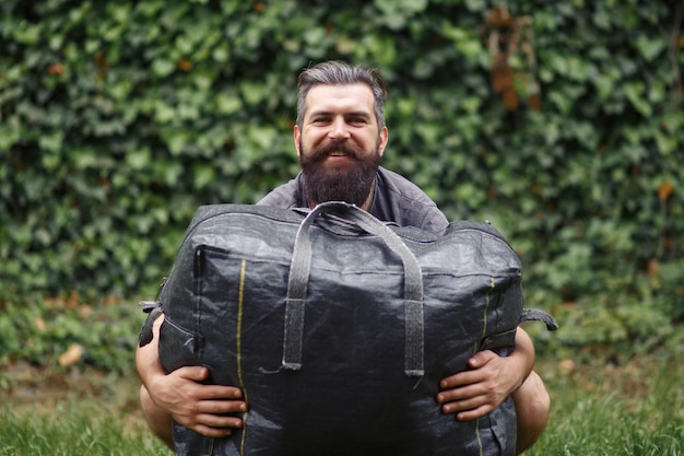 Brutal bearded man courier in shorts and a tshirt is holding a large gray bag the courier is holding a huge parcel