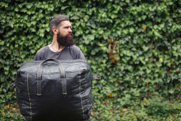 Brutal bearded man courier in shorts and a tshirt is holding a large gray bag the courier is holding a huge parcel