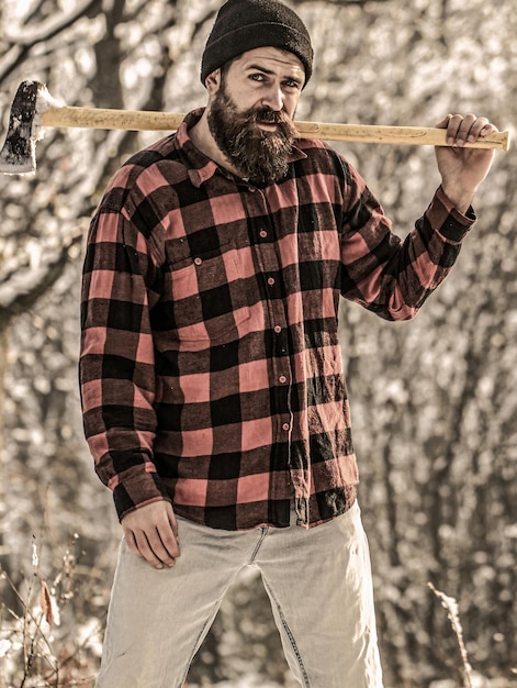 Brutal bearded man with beard and moustache on winter day snowy forest Handsome man hipster lumberjack