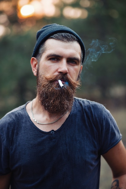 A brutal bearded man with a long beard and mustache in a Tshirt and a warm hat on his shoulder