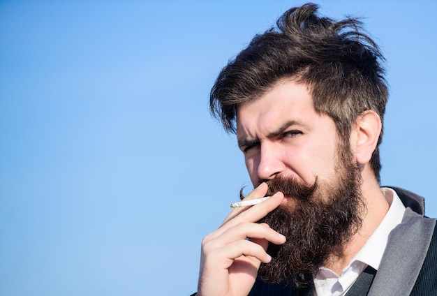 Brutal caucasian hipster with moustache Mature hipster with beard Future success Male formal fashion Bearded man smoking cigarette smoke Businessman against the sky copy space