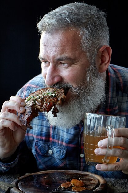 Brutal gray-haired adult man crazy about mustard steak and beer,  holiday, festival, Oktoberfest or St. Patrick's Day