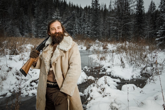 Brutal hunter in winter vintage clothes with beard and gun