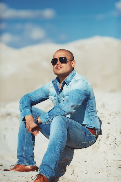 Brutal man sitting on the sand, bronzed