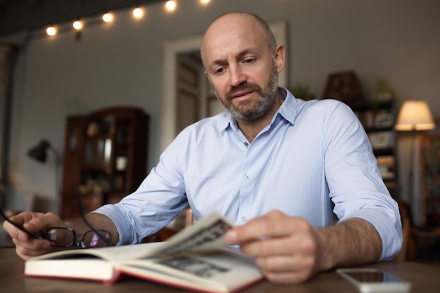 A brutal man with a beard is reading a book sitting at a table resting on the day off Quiet rest after working week at home