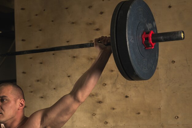 Brutal muscular man with beard train with barbell raised over head in gym