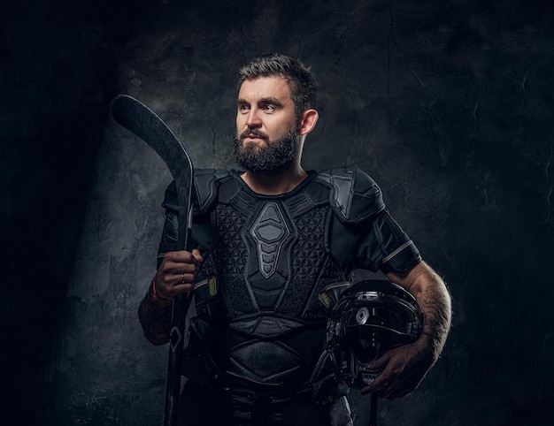 Brutal tattooed hockey player is posing for photographer at dark photo studio.