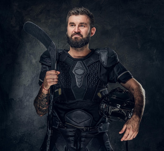 Brutal tattooed hockey player is posing for photographer at dark photo studio.