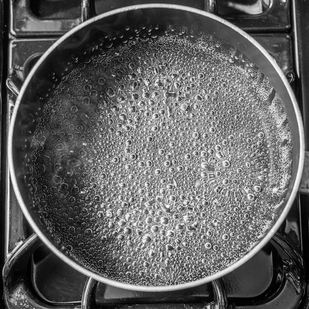 Bubbles and steam of water boiling on black stove.